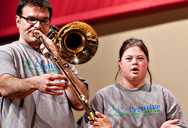SLSO Musician Jonathan Reycraft plays trombone next to clapping woman