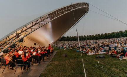 Orchestra playing in bandshell in front of audience sitting outside