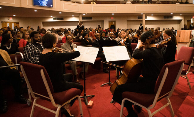 SLSO musicians play string instruments in front of audience in a church