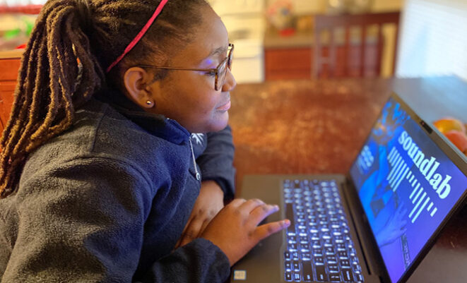 Young girl sitting and using SoundLab digital program on a laptop at home table