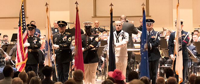 American military members standing on stage holding their respective branch flags