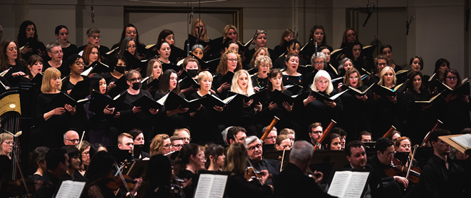 Wide shot of chorus members standing and singing holding choral books. The St. Louis Symphony Chorus is the oldest of our two choruses.