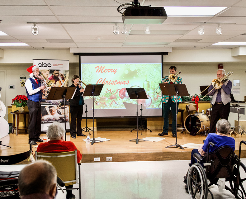 SLSO trombonists play on stage in front of patrons in senior center