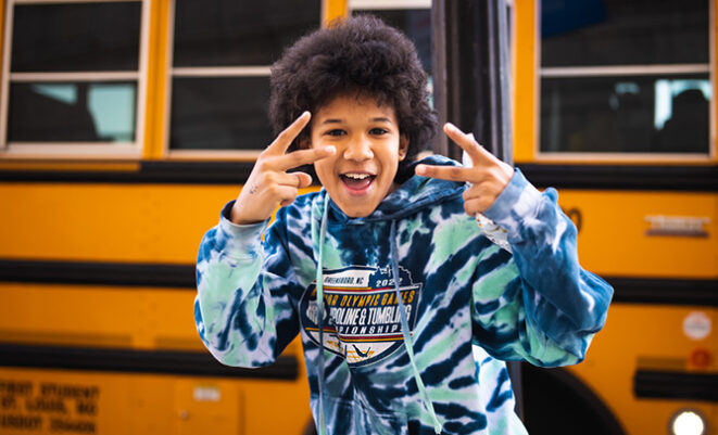 Child doing peace signs in front of a school bus