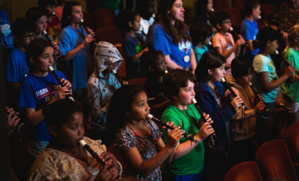 Young students standing and holding recorders in auditorium as part of Link Up program
