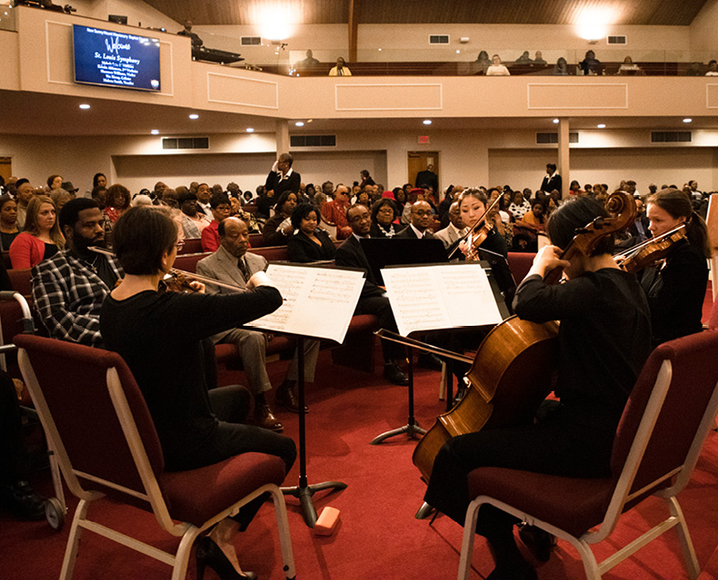 Quartet of string musicians play in front of audience sitting in church