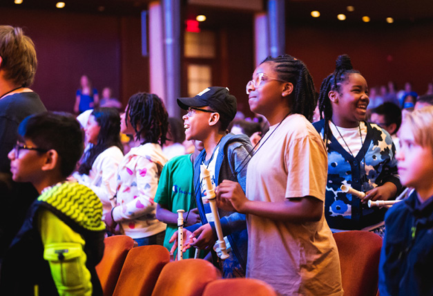 Young students standing and holding recorders in auditorium as part of Link Up program