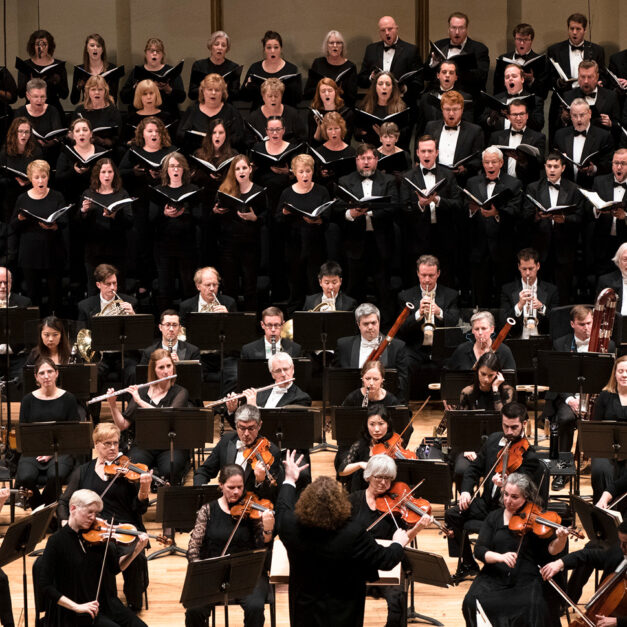 Chorus members singing on stage with the orchestra playing