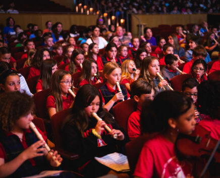 Children sitting and playing recorders in an auditorium as part of the Link Up concert