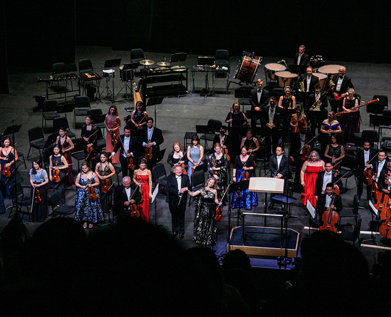 Music Director Stéphane Denève standing on stage with guest artist Hilary Hahn and SLSO musicians after performance