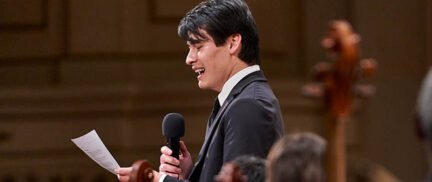 Conductor Norman Huynh speaking on stage into a microphone