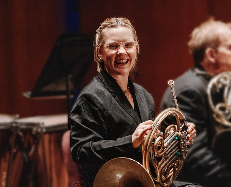 SLSO horn player Victoria Knudtson laughing on stage