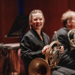 SLSO horn player Victoria Knudtson laughing on stage