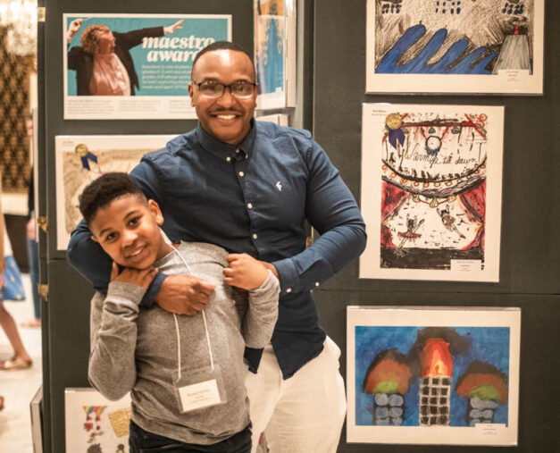 Parent and child posed in front of Picture the Music artwork during award ceremony in foyer