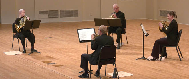 Four SLSO horn players playing on stage